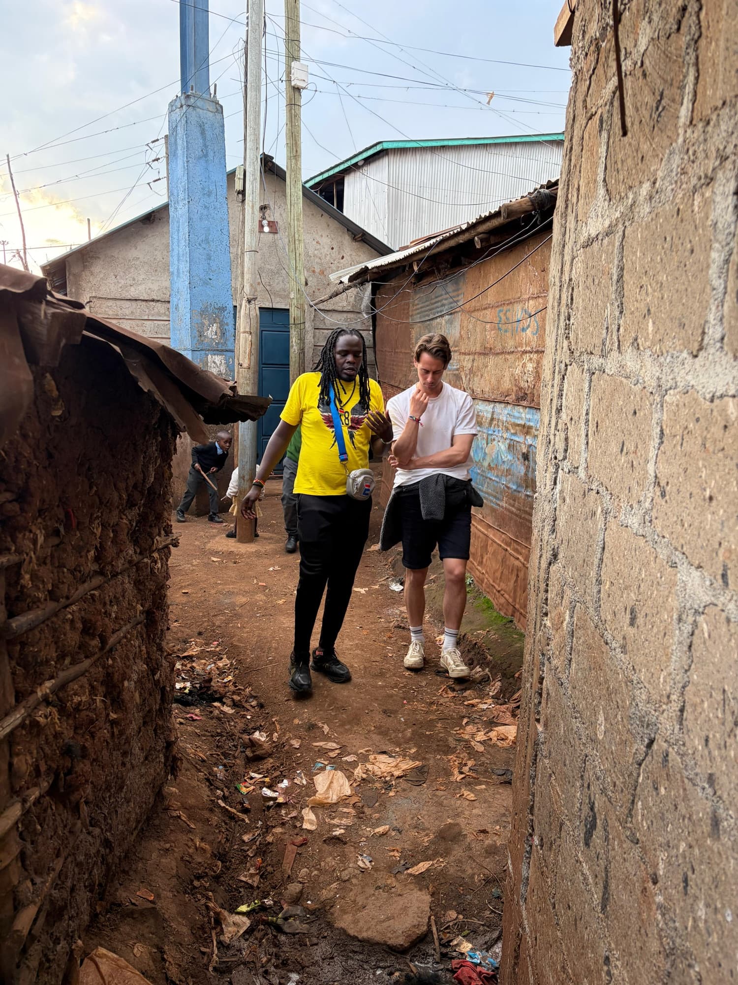 Sammy walking a guest through a narrow lane between houses in Kibera