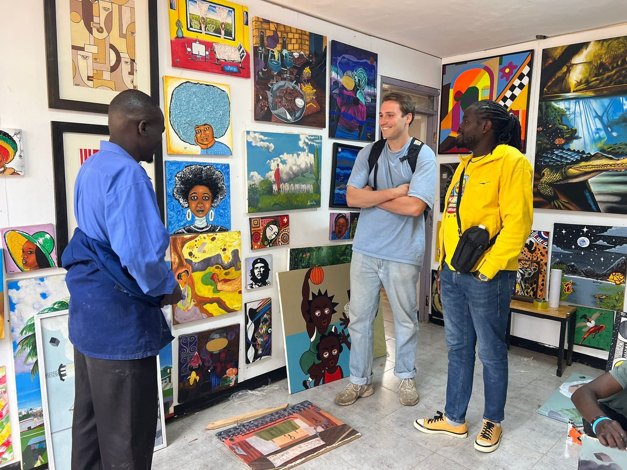 Sammy and a guest talking with an artist in a Kibera gallery hung wall to wall with paintings