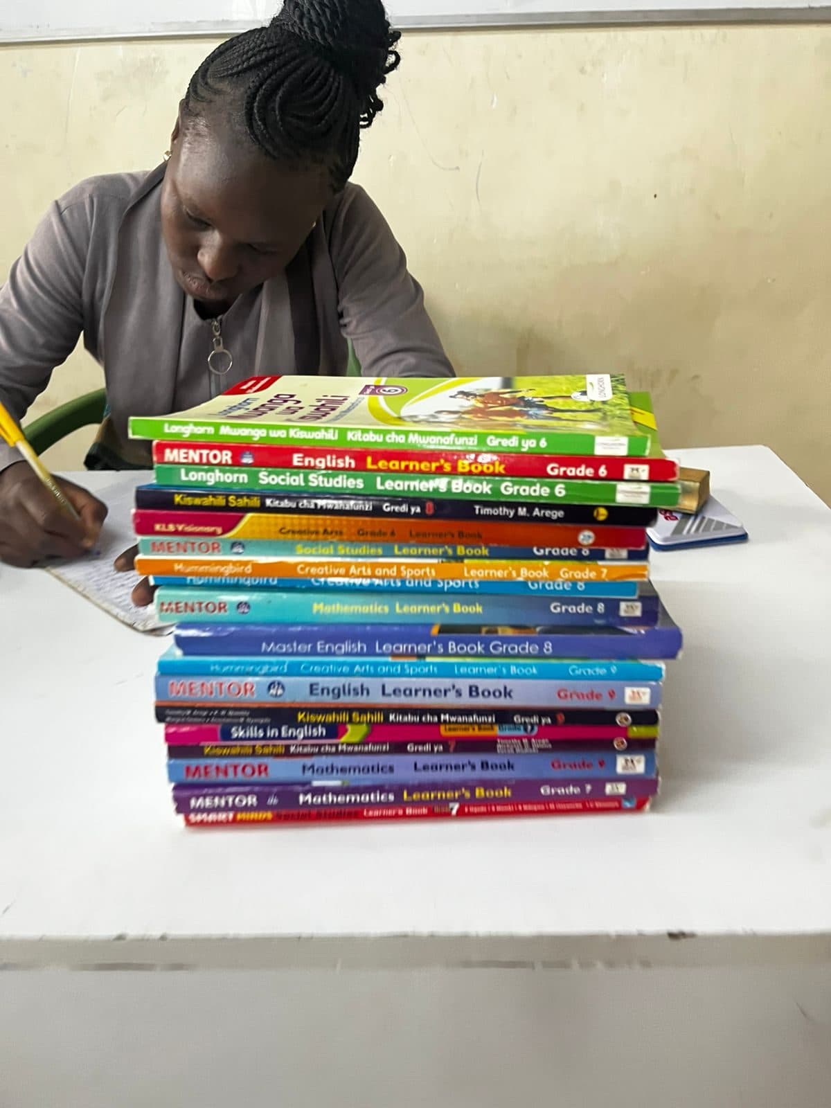 A volunteer writing at a desk beside a stack of new school textbooks