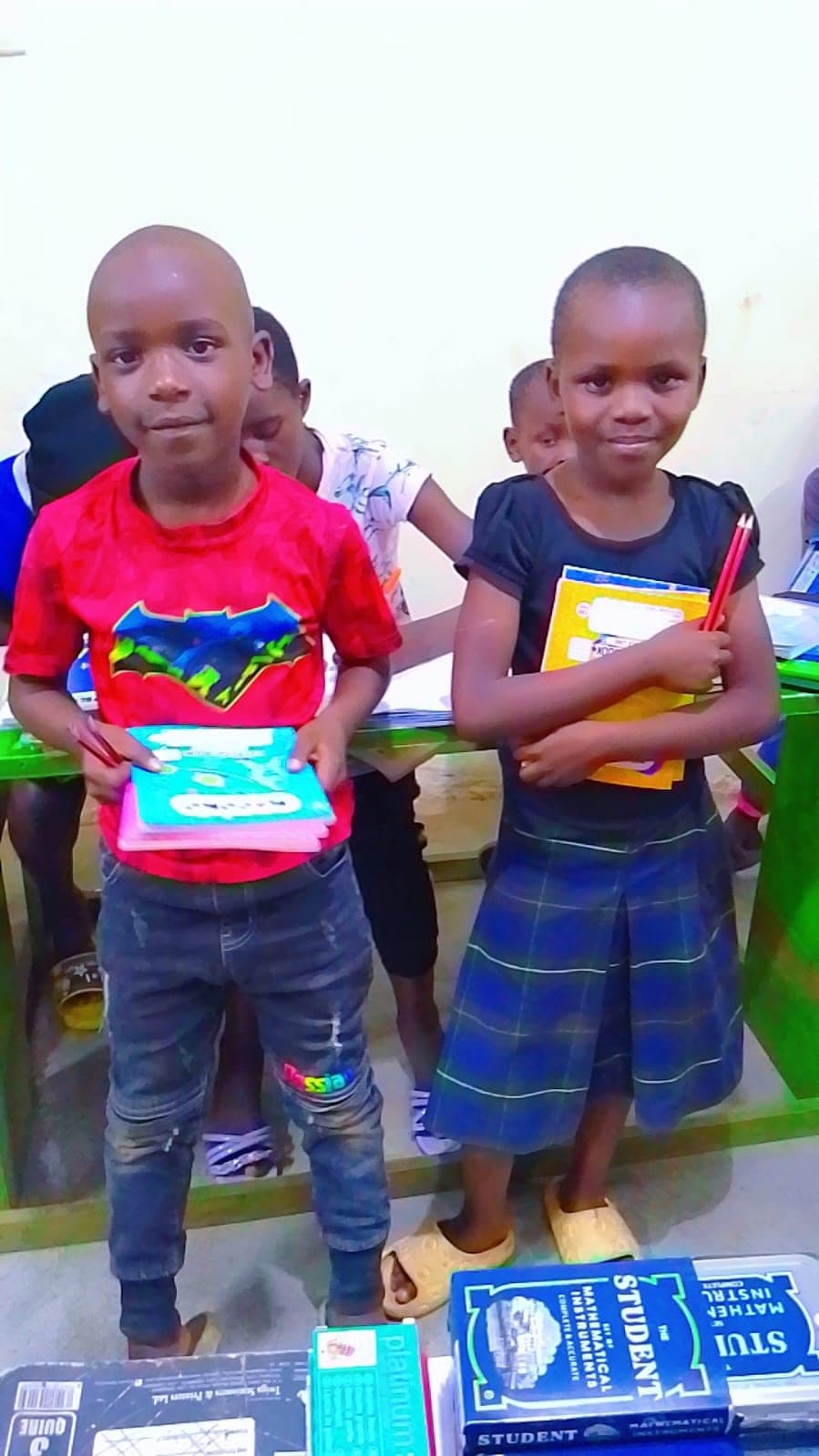 Two children holding the exercise books and pens they were just given