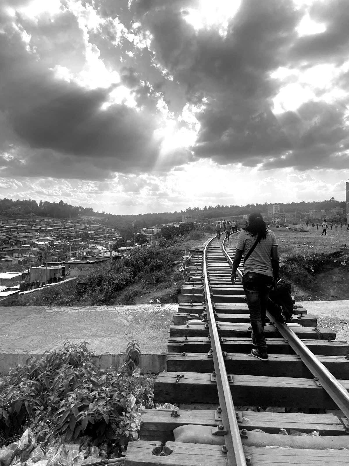 A woman walking up the railway line above Kibera under a heavy sky