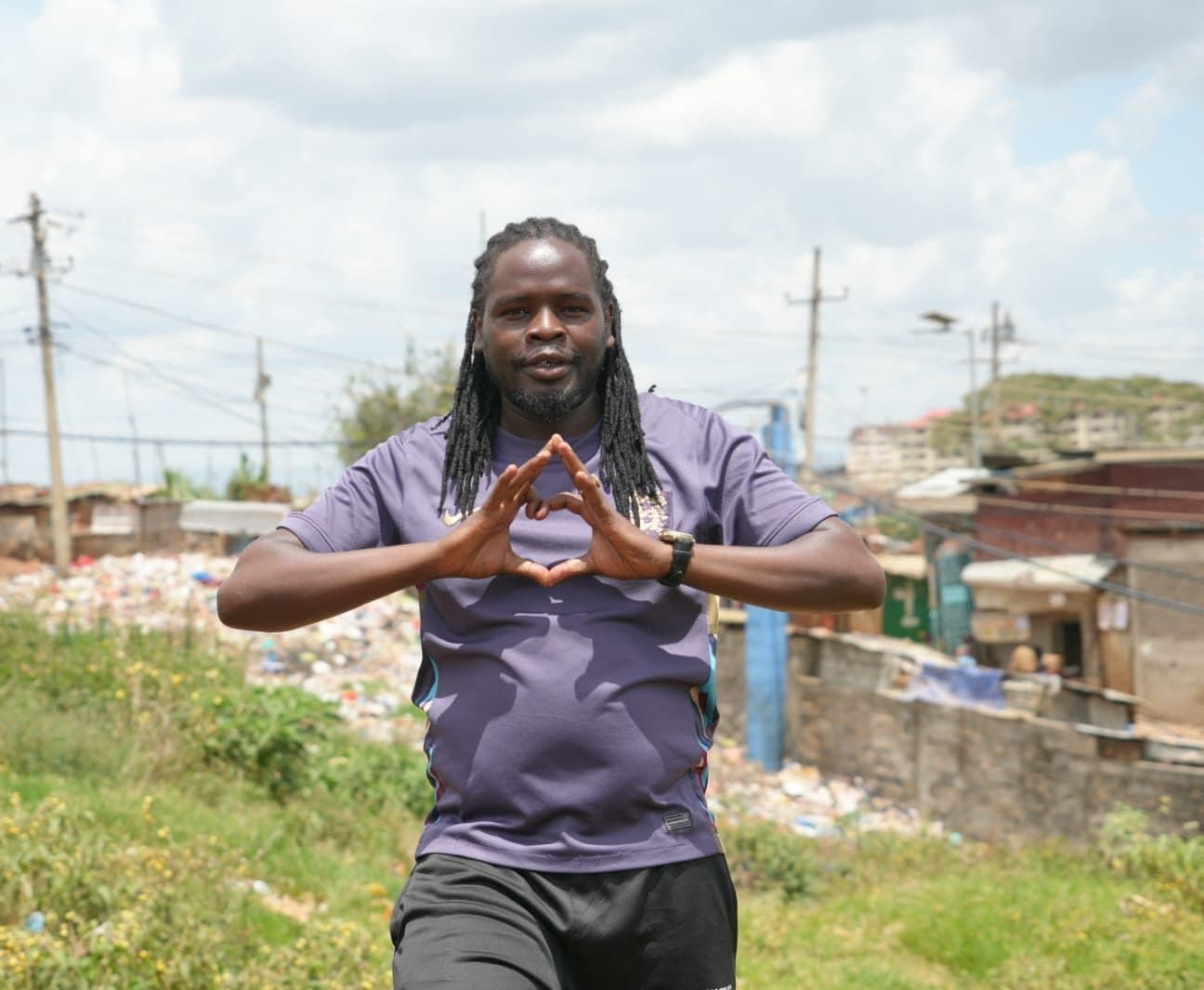 Sammy standing on a path in Kibera, making a heart shape with both hands