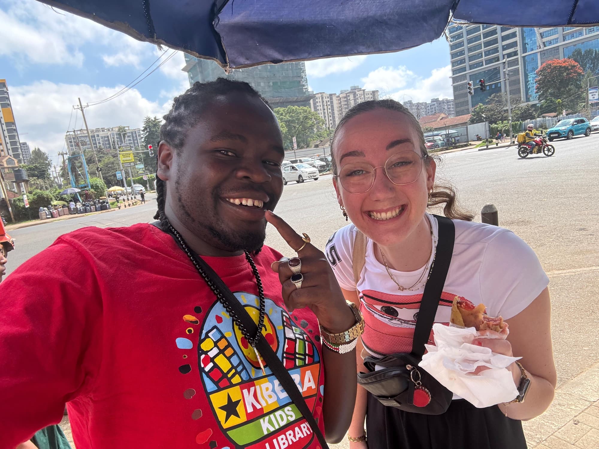Sammy and a guest with street food, the Nairobi skyline behind them