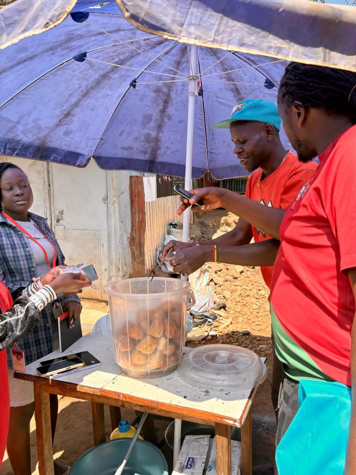 A cook frying snacks at a street stall under a blue umbrella while a guest watches
